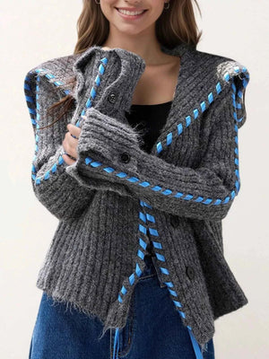 Person wearing a gray knit cardigan with blue accents on a plain background