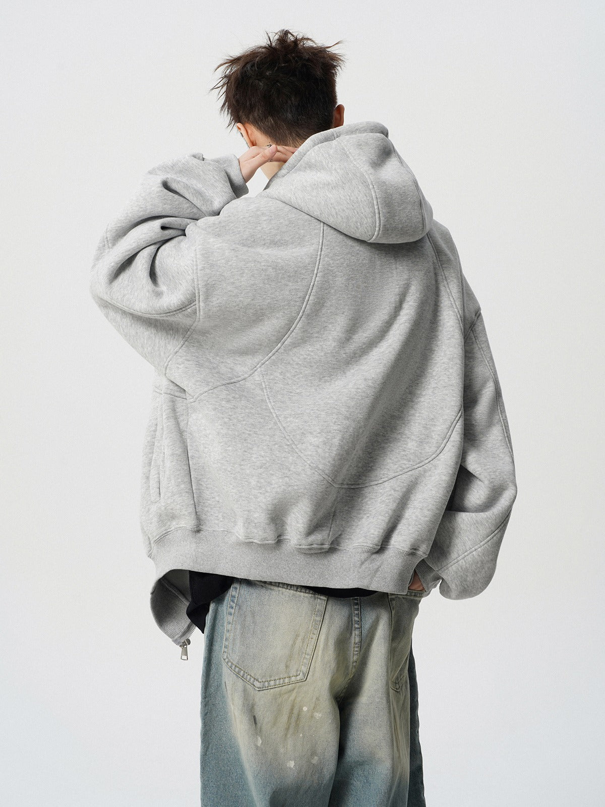 Person wearing a gray hoodie and light blue jeans on a white background