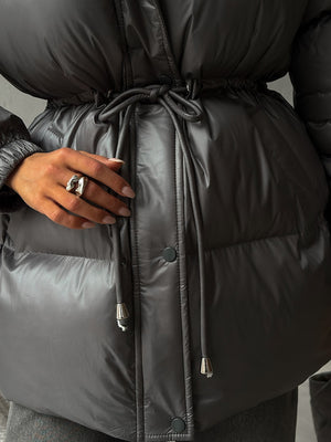 Person wearing a black puffer jacket with a tie waist, focusing on the jacket's design and texture.