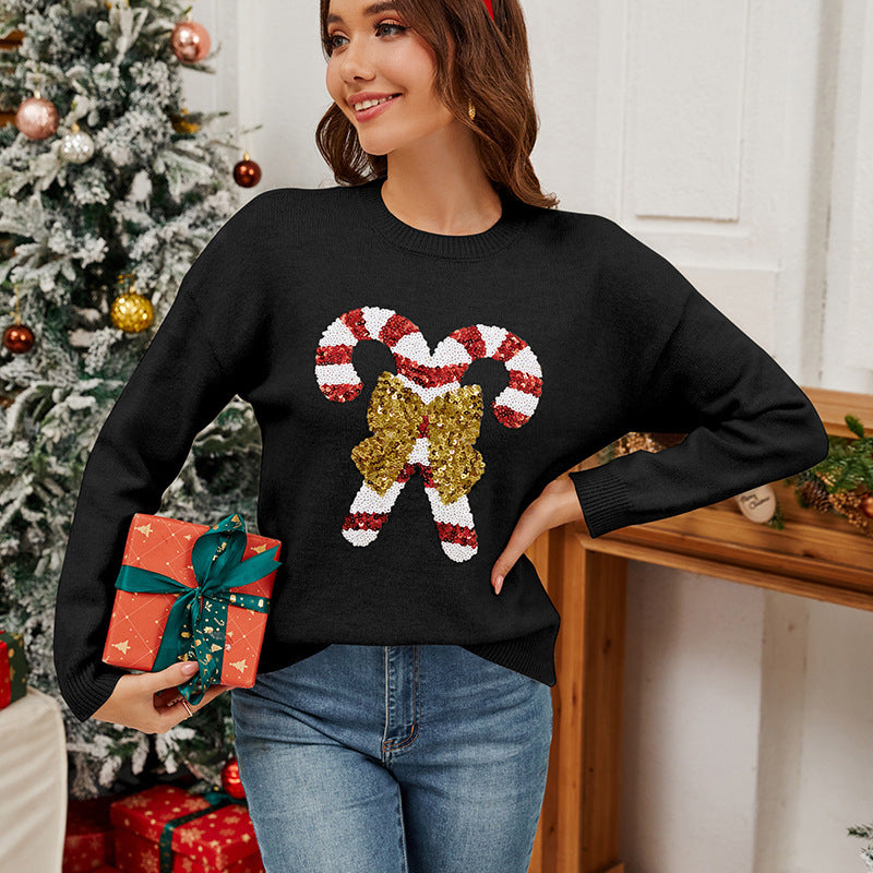 Woman wearing a black sweater with candy cane design, holding a gift, in front of a decorated Christmas tree.
