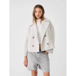 Woman wearing a light gray coat over a white top and denim shorts on a white background