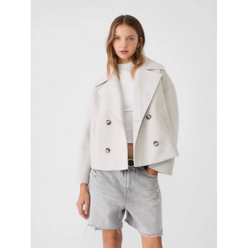 Woman wearing a light gray coat over a white top and denim shorts on a white background