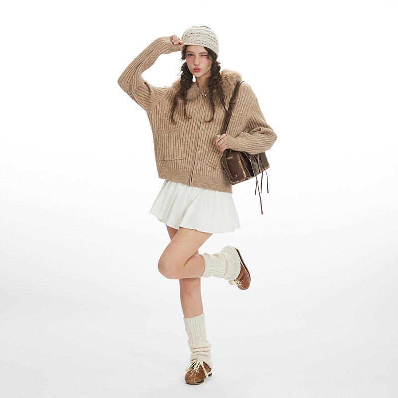 Woman wearing a beige sweater, white skirt, and brown boots on a white background