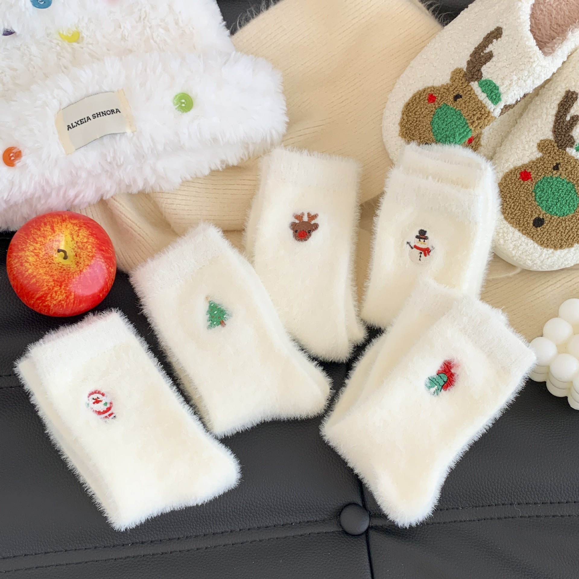 White fuzzy socks with embroidered designs on a black surface, next to an apple.
