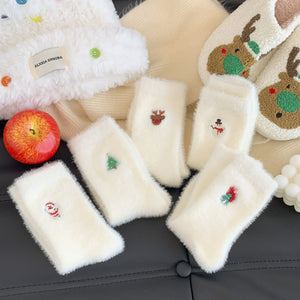 White fuzzy socks with embroidered designs on a black surface, next to an apple.
