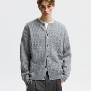 Person wearing a gray cable knit cardigan on a plain background