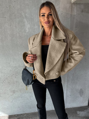 Woman wearing a beige coat and black pants against a gray wall