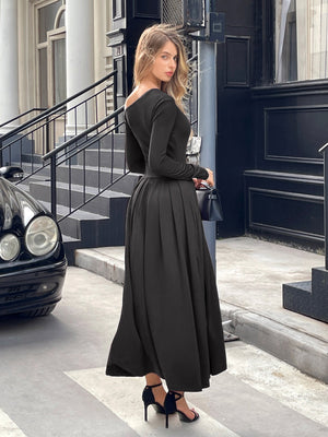 Woman in a black dress standing on a city street with a car and building in the background.