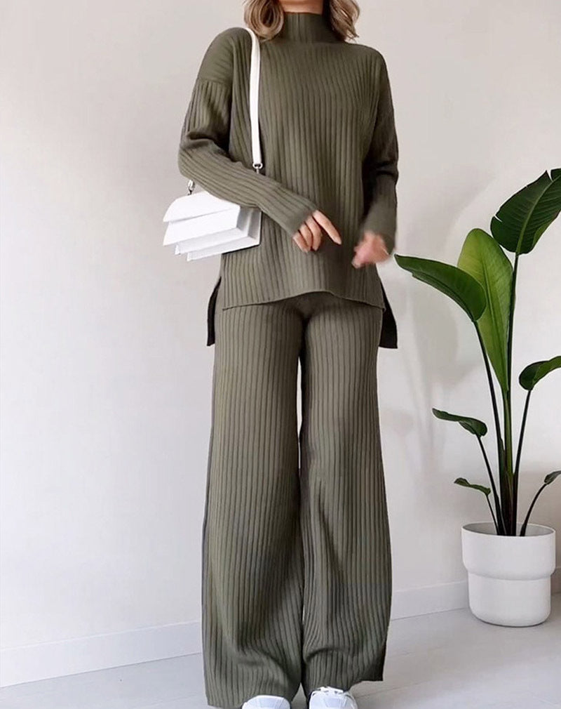 A woman wearing a green knitted turtleneck top and matching straight trousers. Accessories include a white handbag and white shoes.