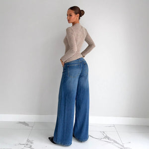 Woman wearing a beige sweater and blue jeans against a white background