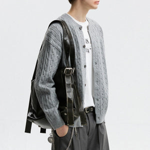 Person wearing a gray knitted cardigan with a black backpack on a light gray background