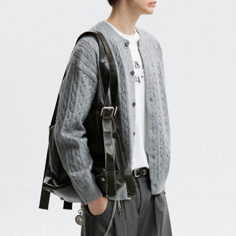 Person wearing a gray knitted cardigan with a black backpack on a light gray background