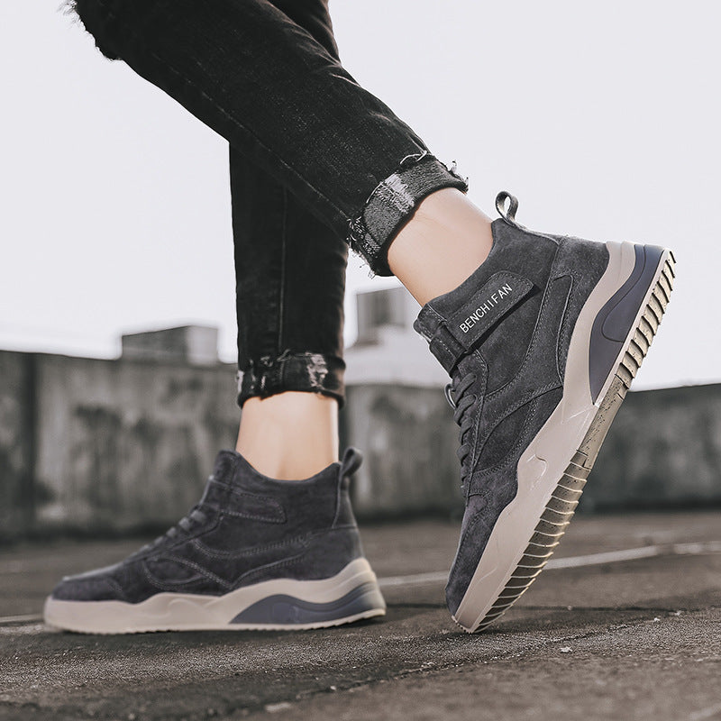 Person wearing dark gray high-top sneakers with beige soles on a blurred background