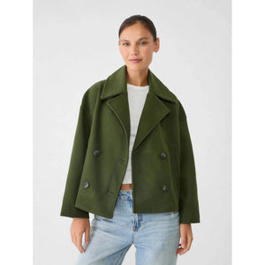 Woman wearing a green coat over a white shirt and blue jeans on a white background