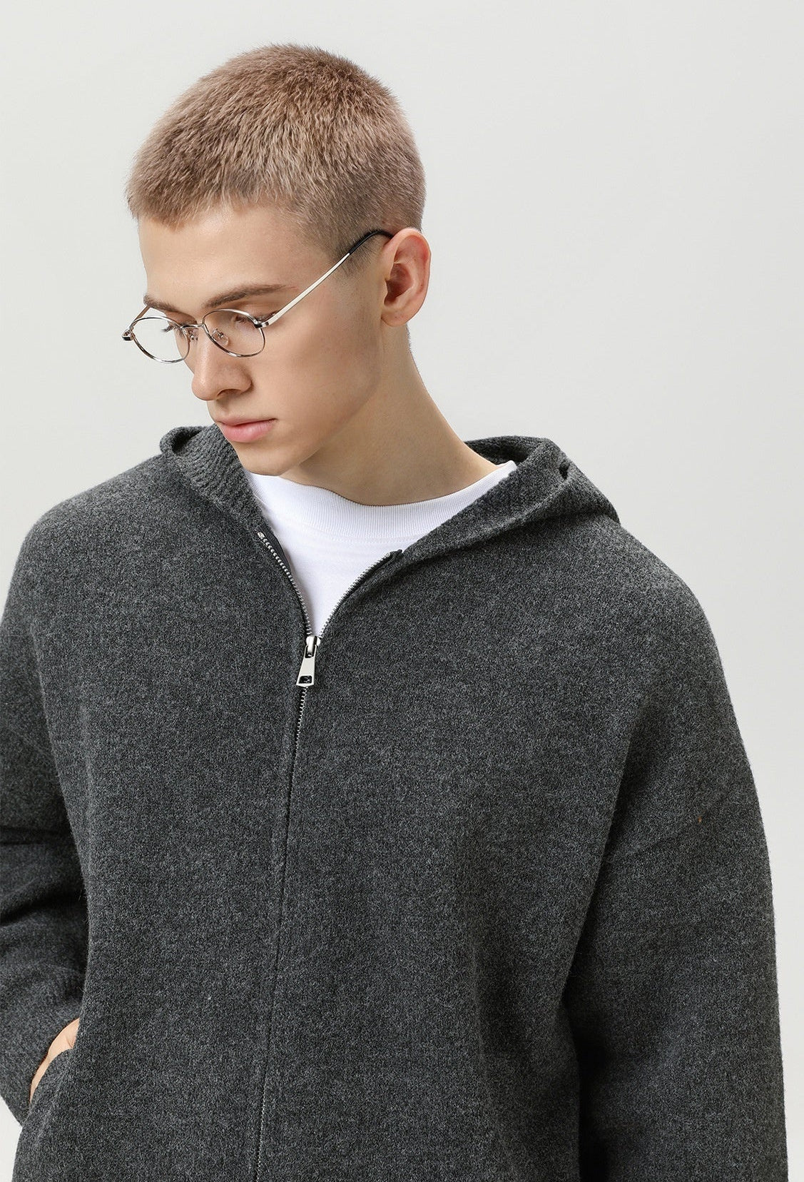 Person wearing a gray zip-up hoodie and glasses on a plain background
