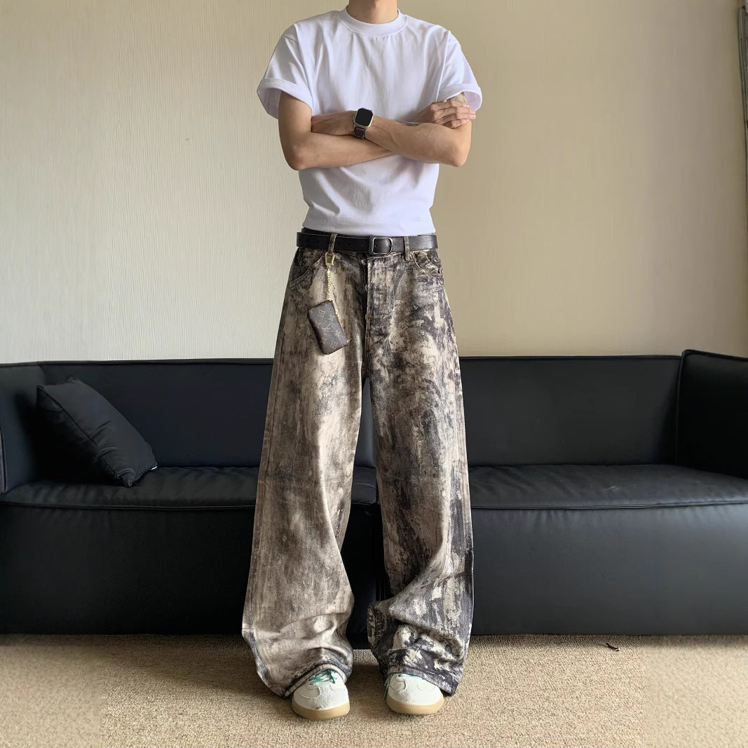 Person wearing a white t-shirt and patterned pants standing in a room with a black sofa.