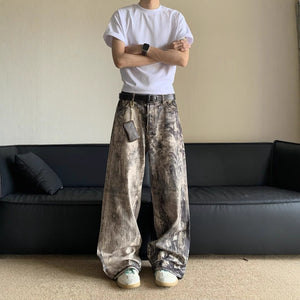 Person wearing a white t-shirt and patterned pants standing in a room with a black sofa.