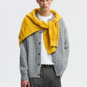 Person wearing a gray cable knit cardigan with a yellow scarf on a white background