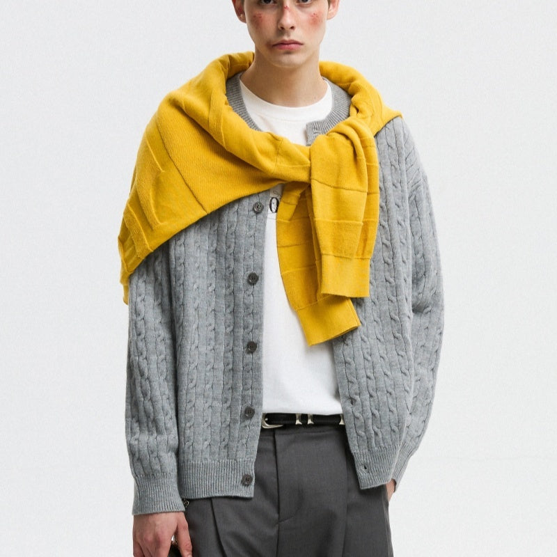 Person wearing a gray cable knit cardigan with a yellow scarf on a white background