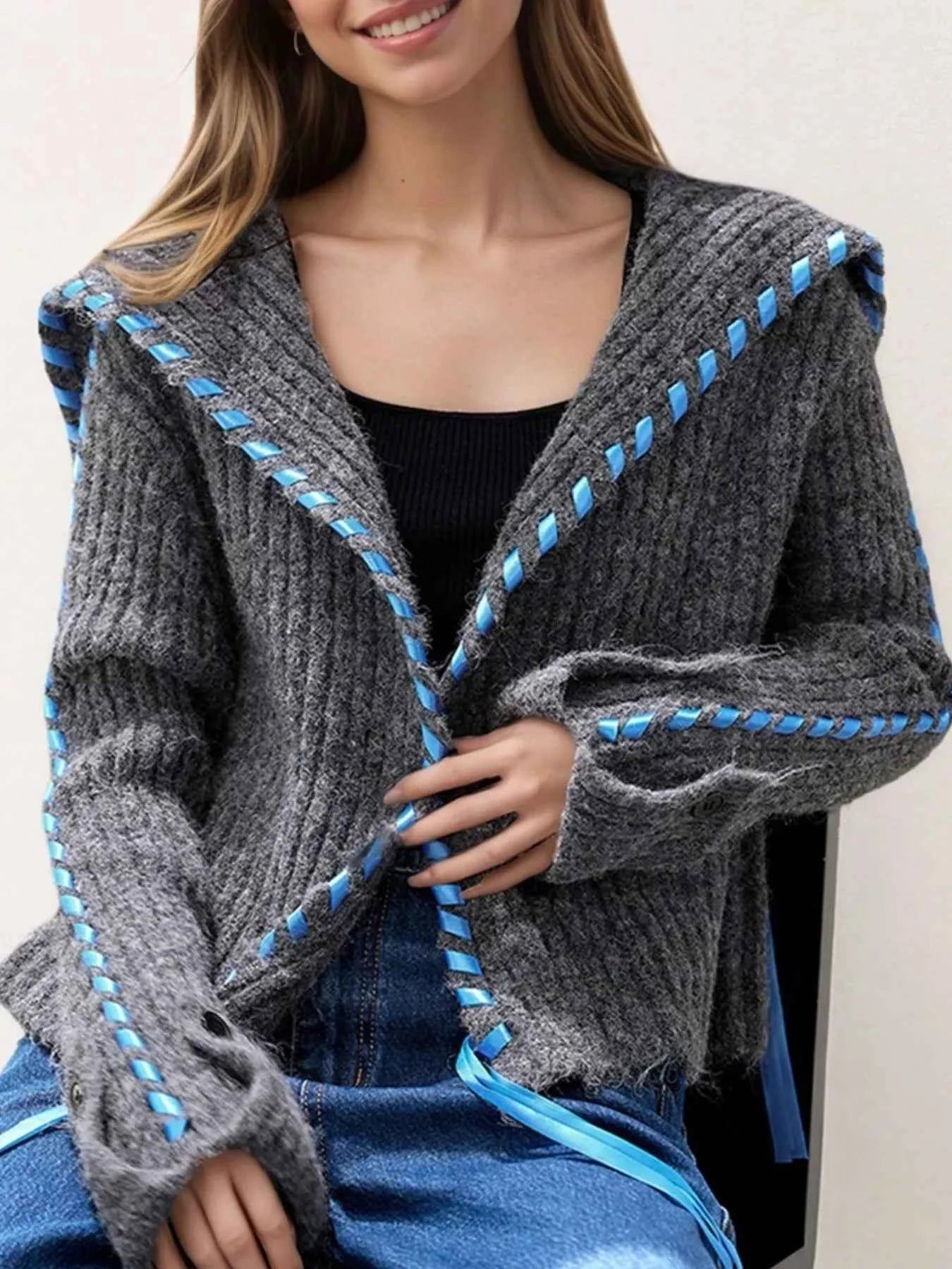 Person wearing a gray knit cardigan with blue accents on a plain background