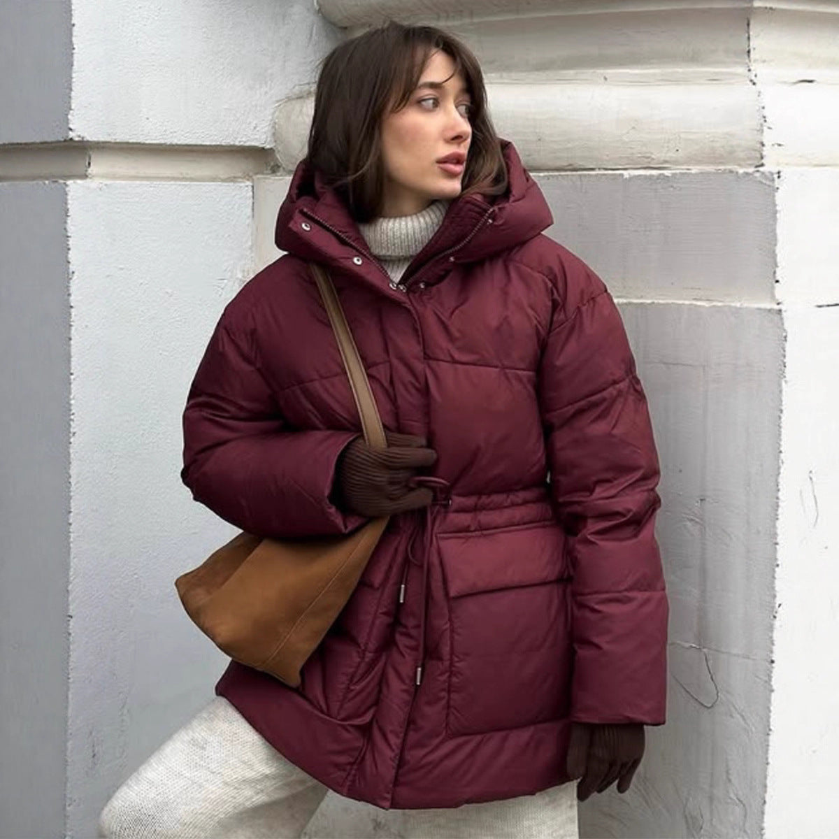 Woman wearing a maroon puffer jacket against a white wall.