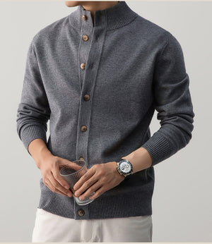 Person wearing a gray cardigan with brown buttons, holding a glass against a plain background