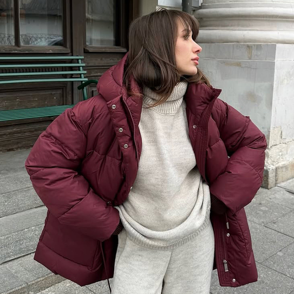 Woman wearing a maroon puffer jacket over a beige sweater and pants on a city street.